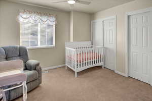 Bedroom featuring a nursery area, multiple closets, light carpet, and a ceiling fan