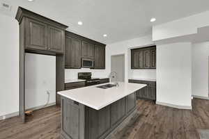 Kitchen featuring range with electric cooktop, a center island with sink, recessed lighting, stainless steel microwave, and dark wood-style flooring