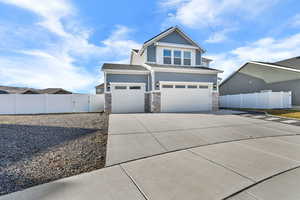 View of front facade with an attached garage, concrete driveway, stone siding, and a gate