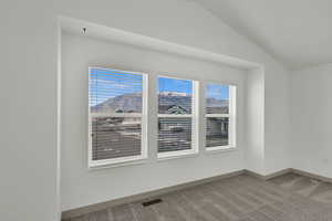 Empty room with light colored carpet, lofted ceiling, and a mountain view