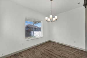 Spare room with dark wood-type flooring and a chandelier