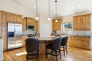 Kitchen featuring appliances with stainless steel finishes, a center island, pendant lighting, light wood finished floors, and a breakfast bar area