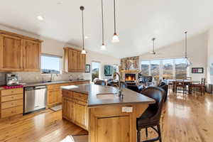 Kitchen with hanging light fixtures, an island with sink, dishwasher, a fireplace, and vaulted ceiling