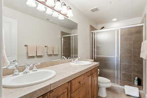 Bathroom featuring double vanity, a stall shower, and light tile patterned floors