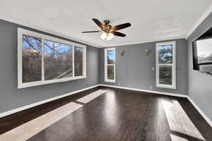 Spare room with crown molding, dark wood-style floors, and ceiling fan