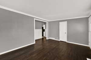 Empty room with dark wood-style flooring and ornamental molding