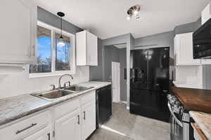 Kitchen with backsplash, black appliances, pendant lighting, and white cabinetry
