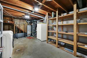 Unfinished basement featuring washer / dryer, freestanding refrigerator, water heater, and heating unit