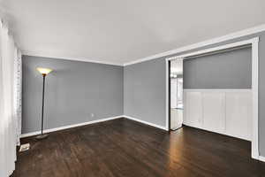 Spare room featuring dark wood-style flooring, crown molding, and a wainscoted wall