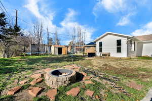 View of grassy yard with a storage unit, a trampoline, and an outdoor fire pit
