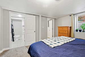 Bedroom with light carpet, a textured ceiling, and connected bathroom
