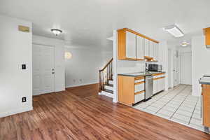 Kitchen with light wood-style flooring, brown cabinets, a textured ceiling, appliances with stainless steel finishes, and white cabinetry