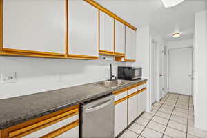 Kitchen with brown cabinetry, white cabinetry, appliances with stainless steel finishes, dark countertops, and light tile patterned floors