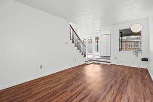 Unfurnished living room with dark wood-style flooring, a textured ceiling, and stairs