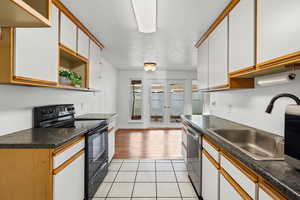 Kitchen featuring brown cabinets, black range with electric stovetop, open shelves, white cabinets, and a textured ceiling