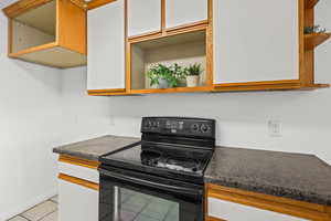 Kitchen featuring open shelves, black / electric stove, dark countertops, and light tile patterned floors