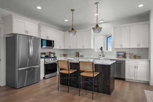 Kitchen featuring appliances with stainless steel finishes, white cabinetry, decorative light fixtures, a center island, and recessed lighting