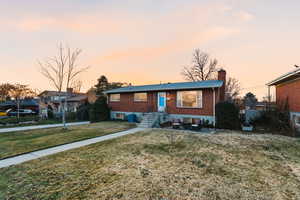View of front of property featuring a chimney, a front yard, and brick siding