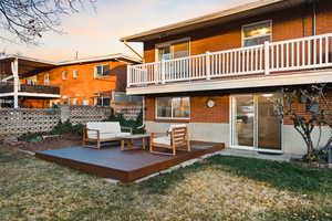 Back of house at dusk with a balcony, a deck, brick siding, and an outdoor hangout area