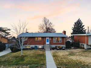 View of front of property featuring brick siding, a chimney, a front lawn, and entry steps