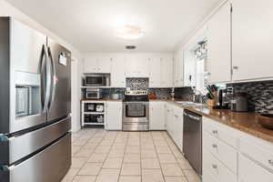 Kitchen with appliances with stainless steel finishes, white cabinetry, light tile patterned flooring, and decorative backsplash