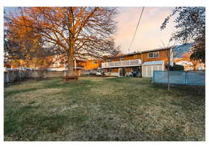 Yard at dusk with a fenced backyard, a balcony, and a patio