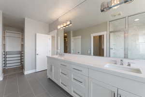 Full bathroom featuring a spacious closet, double vanity, a marble finish shower, and dark tile patterned floors