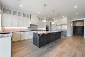 Kitchen with a breakfast bar, stainless steel appliances, pendant lighting, light stone counters, and a center island with sink