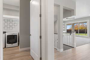 Hall with an upstairs landing, washer and dryer, and light wood finished floors