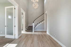 Entrance foyer featuring wood tiled floors, stairs, a chandelier, and a high ceiling