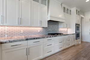 Kitchen with premium range hood, glass insert cabinets, light stone counters, and white cabinets