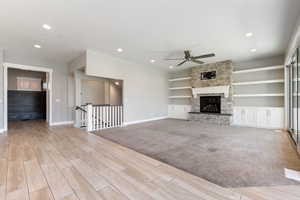Unfurnished living room with wood finish floors, a stone fireplace, a ceiling fan, recessed lighting, and built in shelves