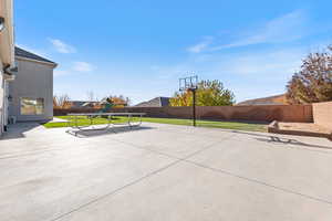 Fenced backyard with a playground, a patio, and basketball hoop