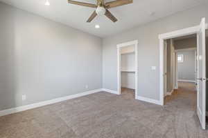 Unfurnished bedroom featuring light colored carpet, a ceiling fan, a spacious closet, and recessed lighting