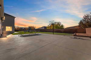 Patio terrace at dusk with a fenced backyard, a playground, a trampoline, and a patio