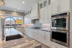 Kitchen featuring stainless steel appliances, glass insert cabinets, white cabinets, decorative light fixtures, and light stone countertops