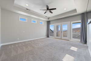 Unfurnished room featuring a tray ceiling, french doors, healthy amount of natural light, light colored carpet, and recessed lighting