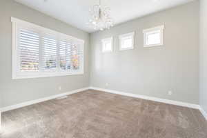 Empty room with healthy amount of natural light, light colored carpet, and a chandelier