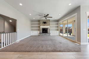 Unfurnished living room with built in features, ceiling fan, a fireplace, recessed lighting, and light colored carpet