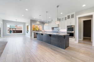 Kitchen featuring glass insert cabinets, a breakfast bar area, an island with sink, white cabinets, and stainless steel double oven