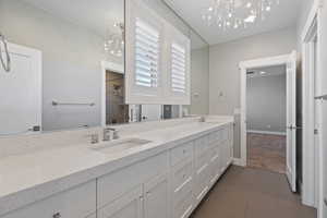Full bathroom with double vanity, a chandelier, dark tile patterned floors, dark colored carpet, and tiled shower