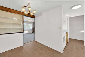 Unfurnished dining area featuring a chandelier, light tile patterned flooring, and light colored carpet