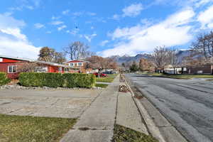 View of asphalt road featuring sidewalks, a residential view, a mountain view, and curbs