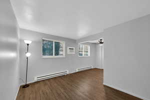 Front room with a baseboard heating unit, brand new LVP flooring, a wall mounted AC, and a ceiling fan