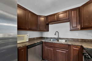 Kitchen with new stainless steel appliances, dark countertops, and dark wood cabinets