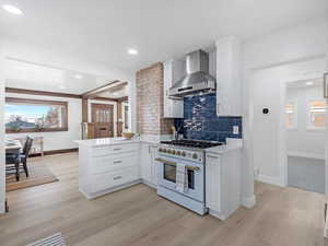 Kitchen featuring healthy amount of natural light, white cabinetry, high end white high end range oven, wall chimney exhaust hood, and recessed lighting