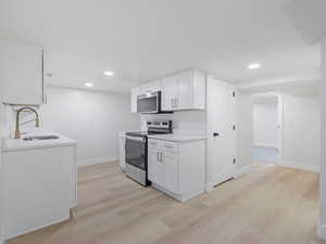 Basement Kitchen with white cabinets, stainless steel appliances, light wood-type flooring, recessed lighting, and light stone counters