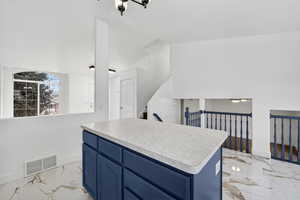 Kitchen with blue cabinets, light marble finish flooring, light countertops, and a center island