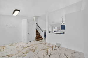 Spare room with a chandelier, stairs, light marble finish floors, and lofted ceiling
