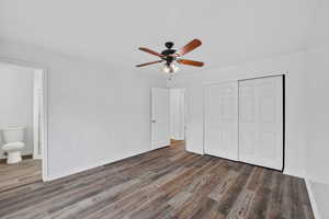 Unfurnished bedroom featuring dark wood finished floors, ceiling fan, a closet, and ensuite bathroom